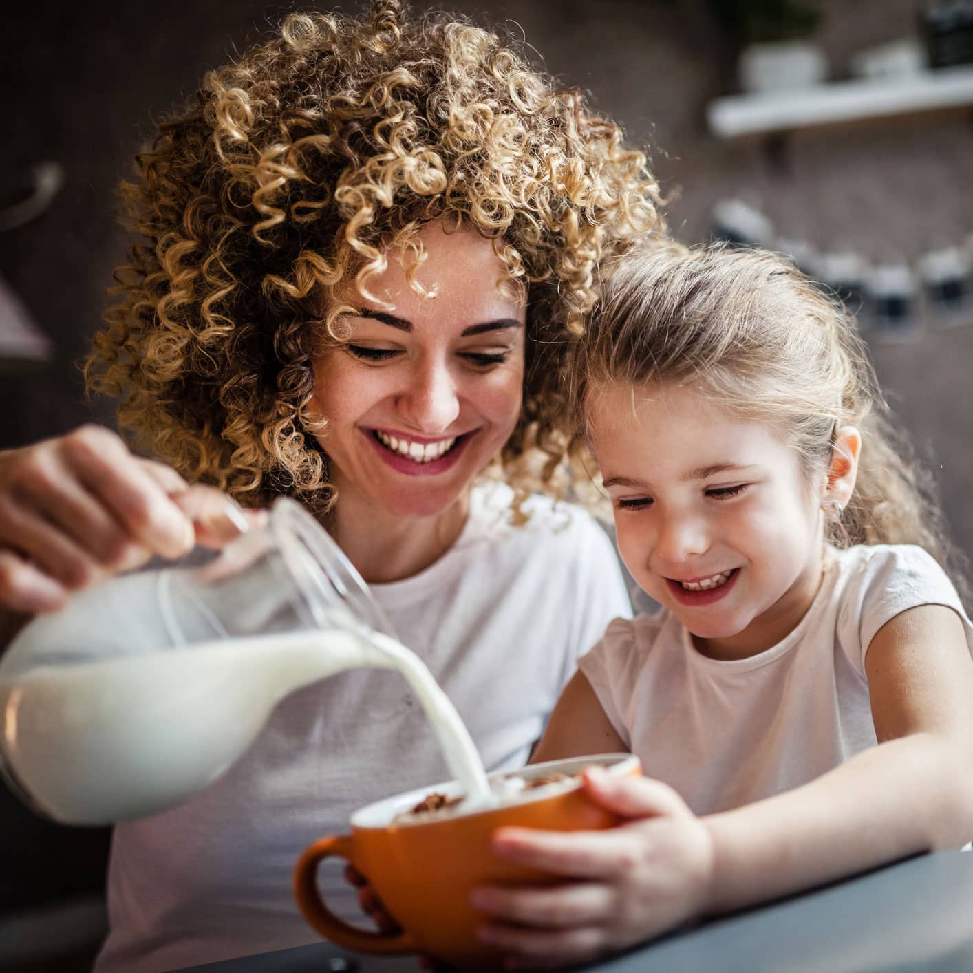 mom pours milk into cereal bowl for daughter